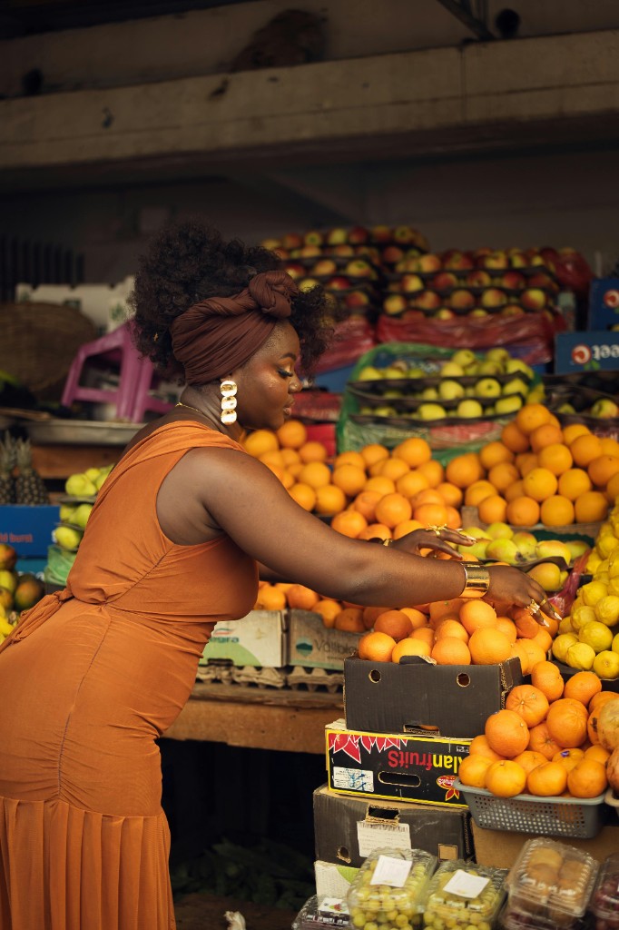 African woman at a vibrant market selecting fresh oranges